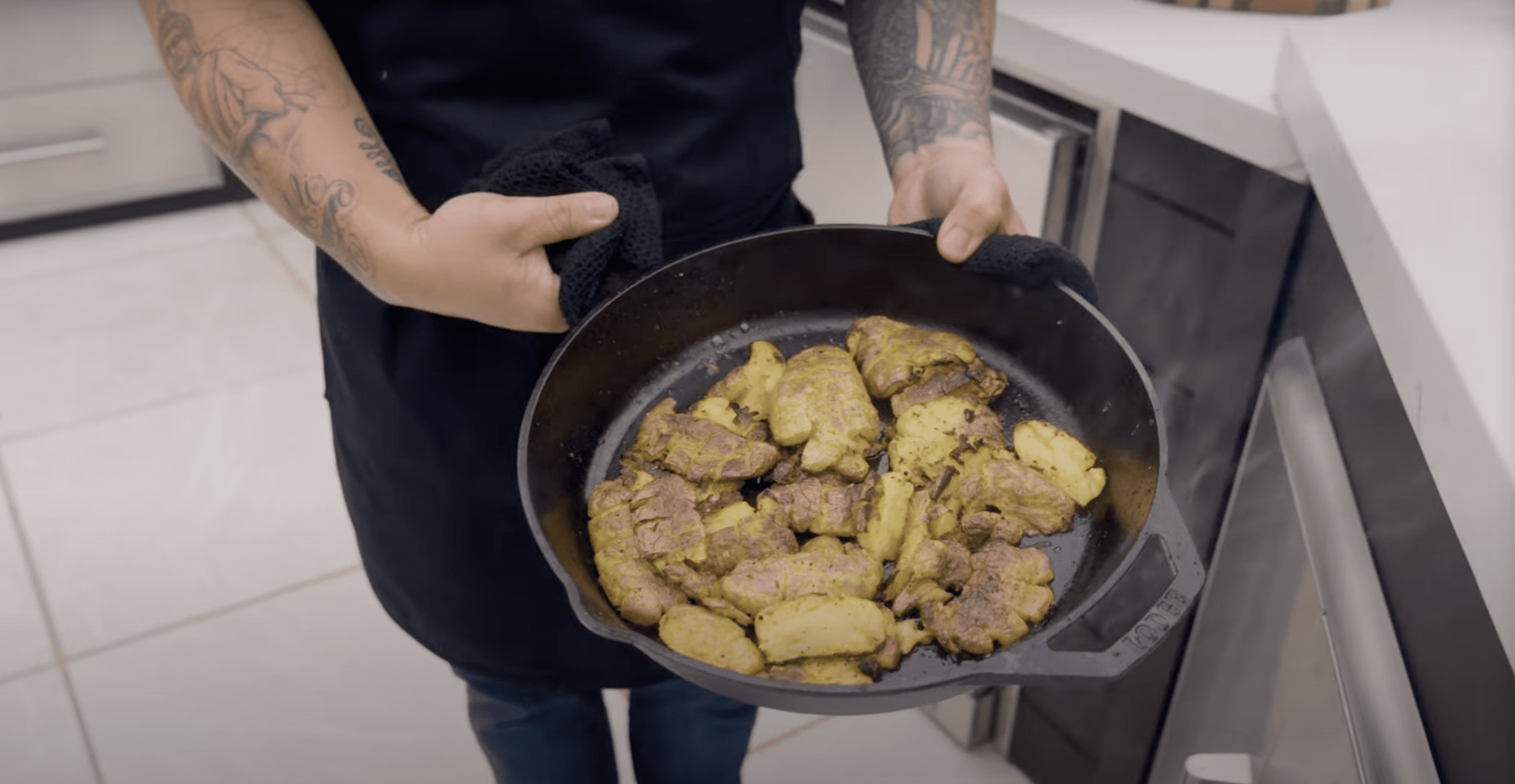 Jet Tila's arms holding a cast iron skillet with smashed potatoes in it